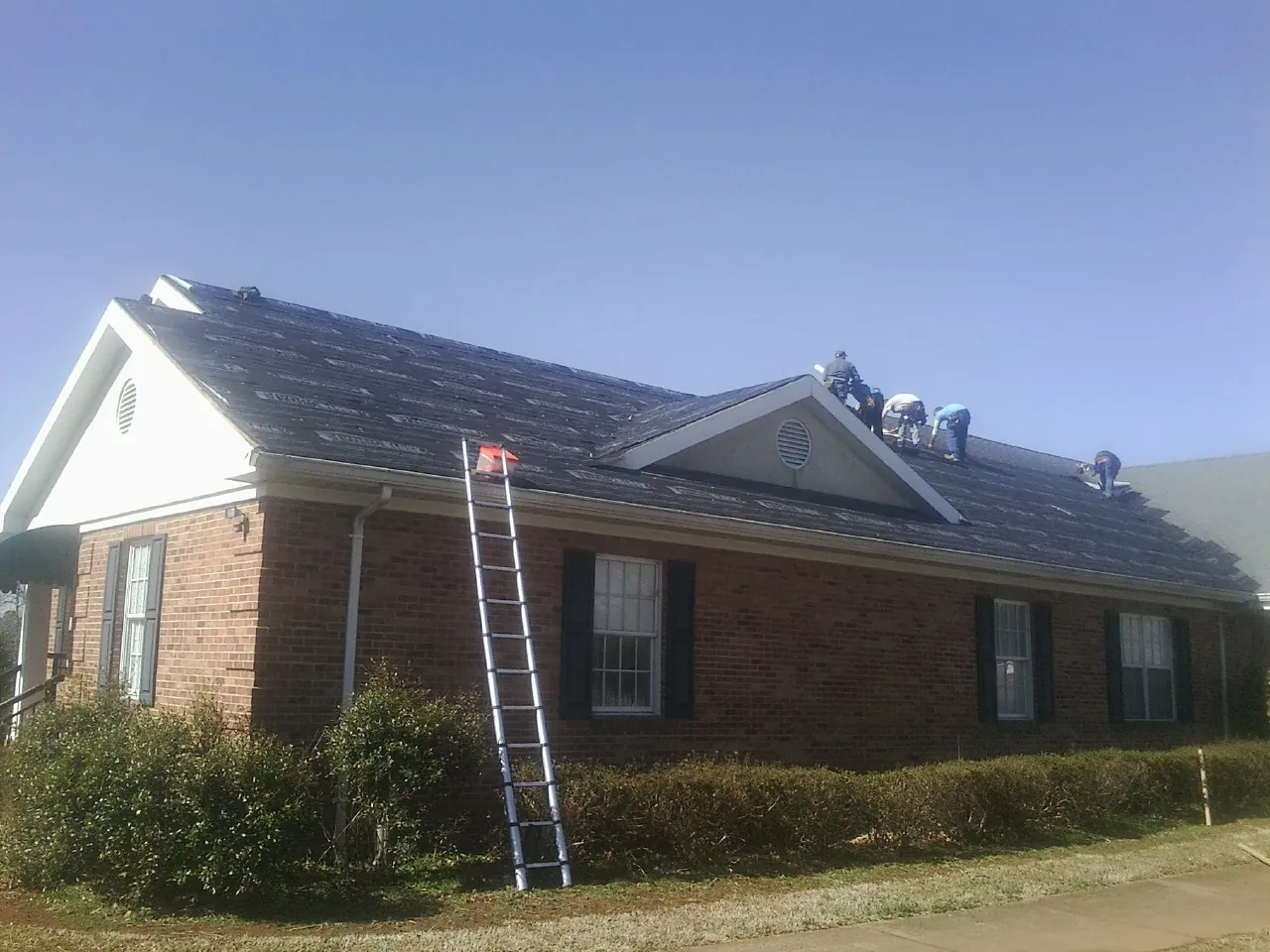 Crew tearing shingles off a brick ranch roof with a ladder set — Emergency Roof Repair work by our crew in Keyport