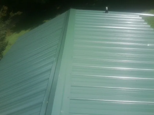 New green metal panels meeting at the ridge of a roof — Flat Roof Repair work by our crew in Keyport