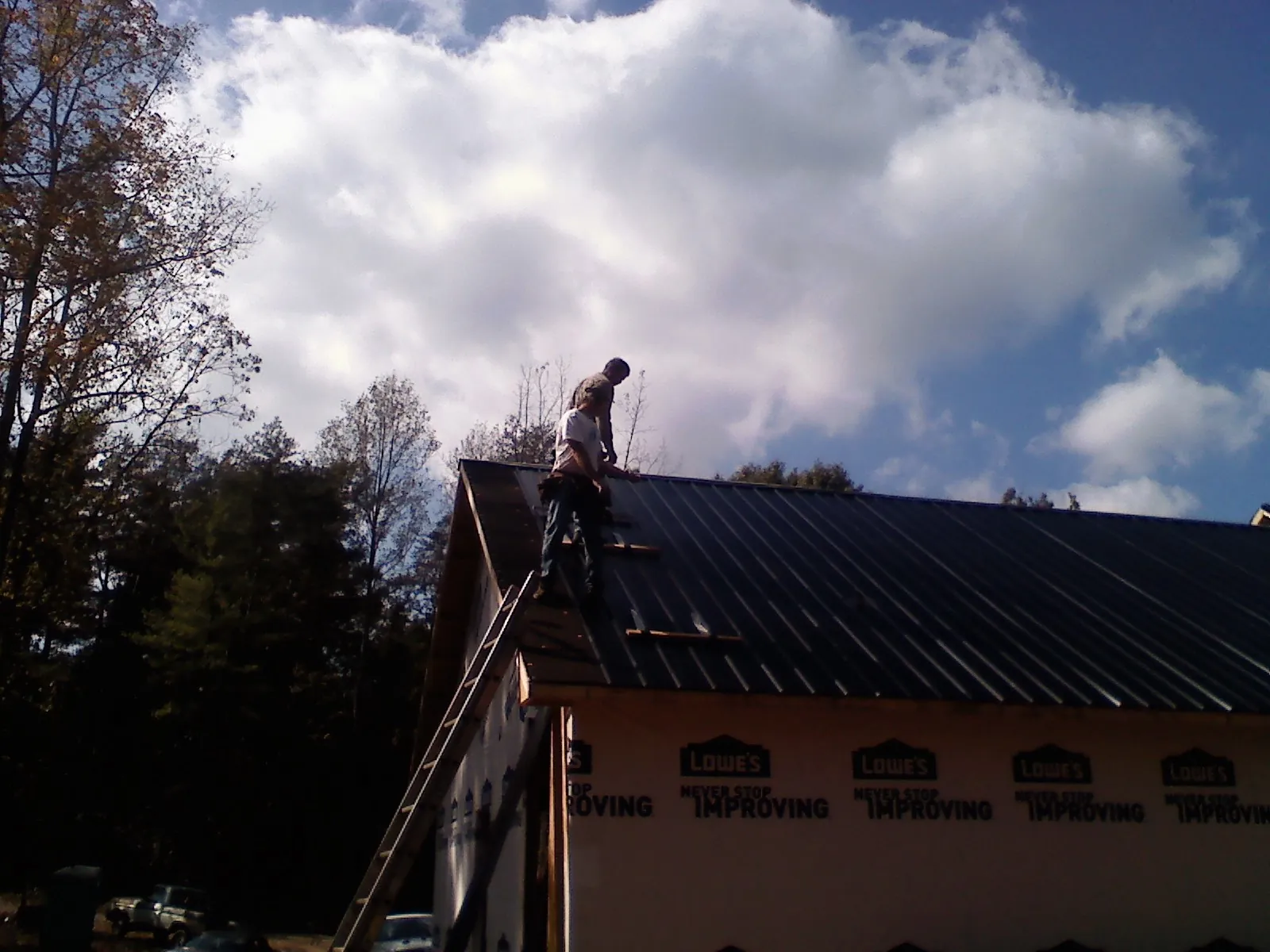 Roofer fastening dark metal panels high against a cloudy sky, from a Roof Inspection job in Keyport