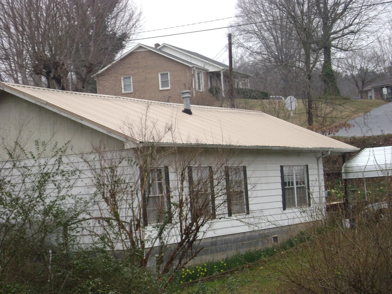 Tan metal roof on a white sided house set into a hillside — Commercial Roofing by Roofing Brothers in Keyport